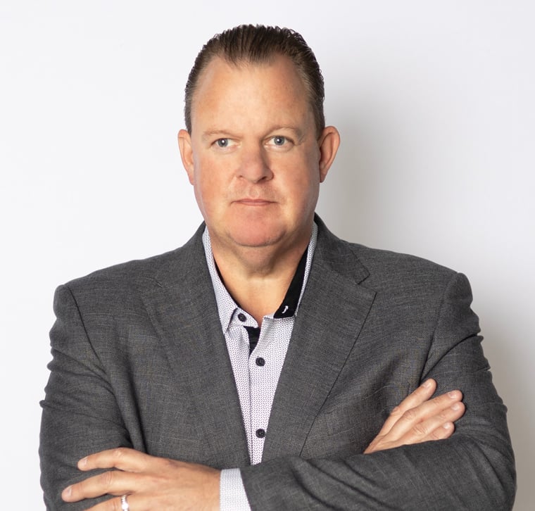 Man in a gray suit jacket with arms crossed, standing in front of a plain white background.