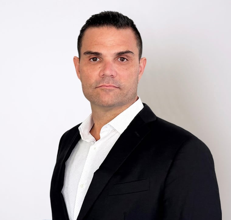 Man wearing a black suit jacket and white shirt, standing against a plain white background, facing forward with a neutral expression.