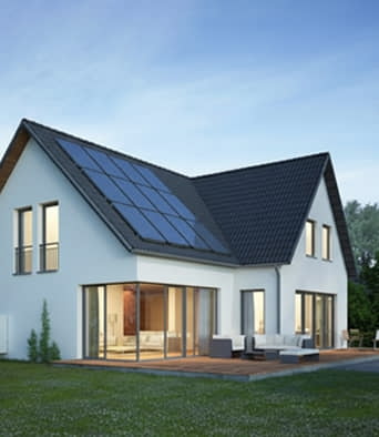 Modern two-story house with large windows, a dark sloped roof, solar panels, and a patio furnished with outdoor seating, set on a grassy lawn under a clear sky.