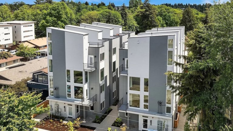 Aerial view of modern, multi-story townhouse buildings with large windows and balconies, surrounded by trees and neighboring residences.