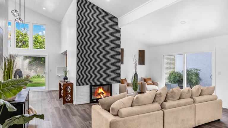 Modern living room with beige sectional sofa, fireplace with wavy black accent wall, large windows, sliding glass door, and wood flooring.